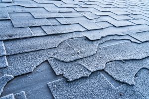 Close up view on Asphalt Roofing Shingles roof damage covered with frost.